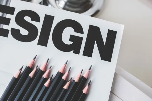 A piece of paper with the word Design is shown with pencils on top of it